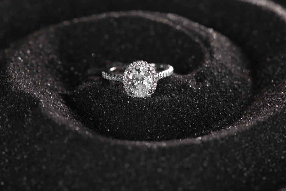 An engagement ring with a large central diamond and smaller diamonds along the band, placed on black textured material.