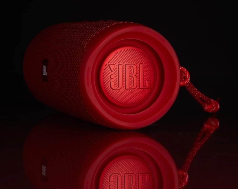 Red JBL portable Bluetooth speaker with a wrist strap, lying on a black reflective surface.