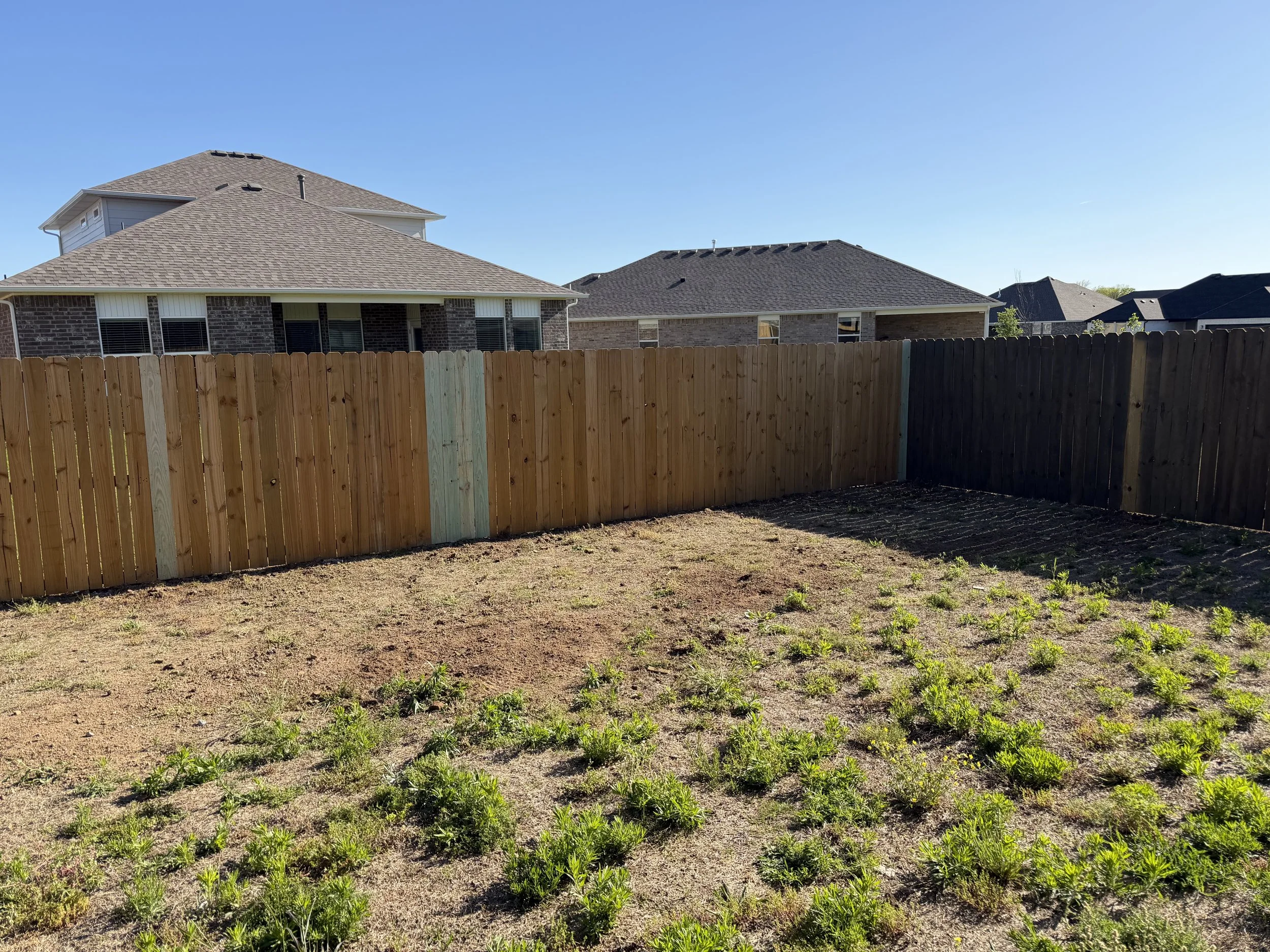 Repaired wood privacy fence with new pressure-treated sections in a Fayetteville backyard.