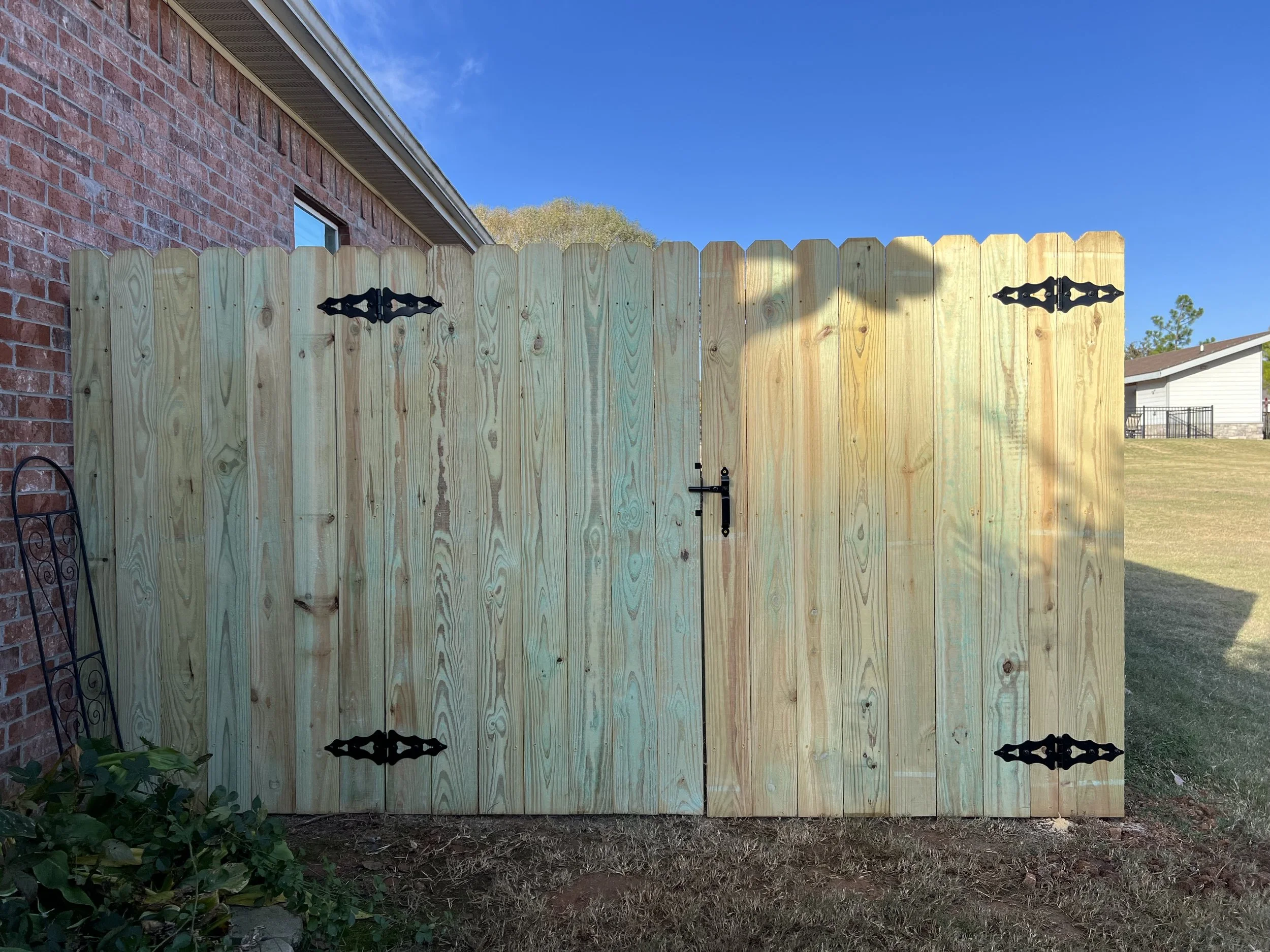Custom pressure-treated pine double gate with black hardware installed in Fayetteville, Arkansas.