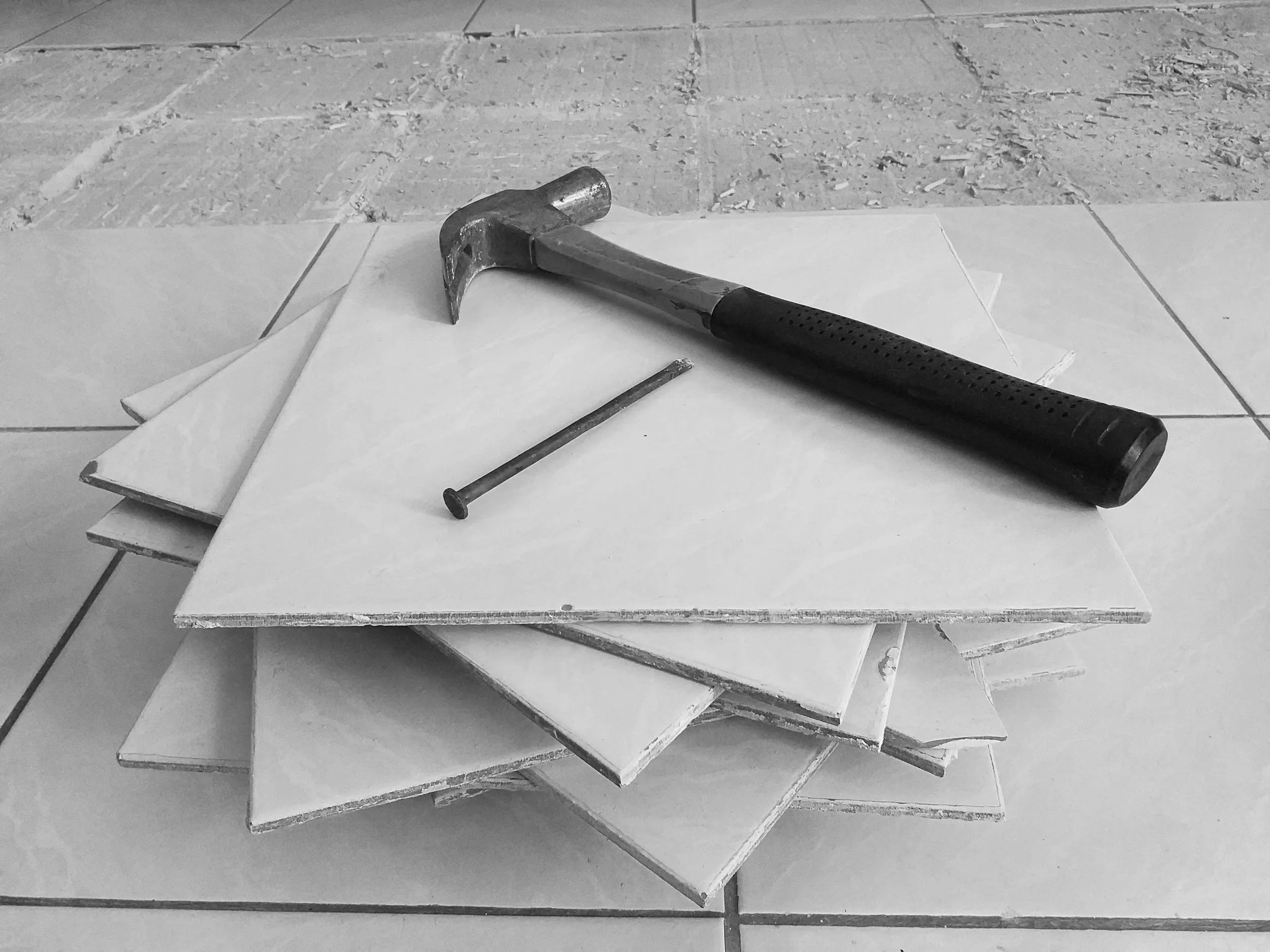 A pile of white ceramic tiles with a hammer and a nail on top, on a tiled floor.