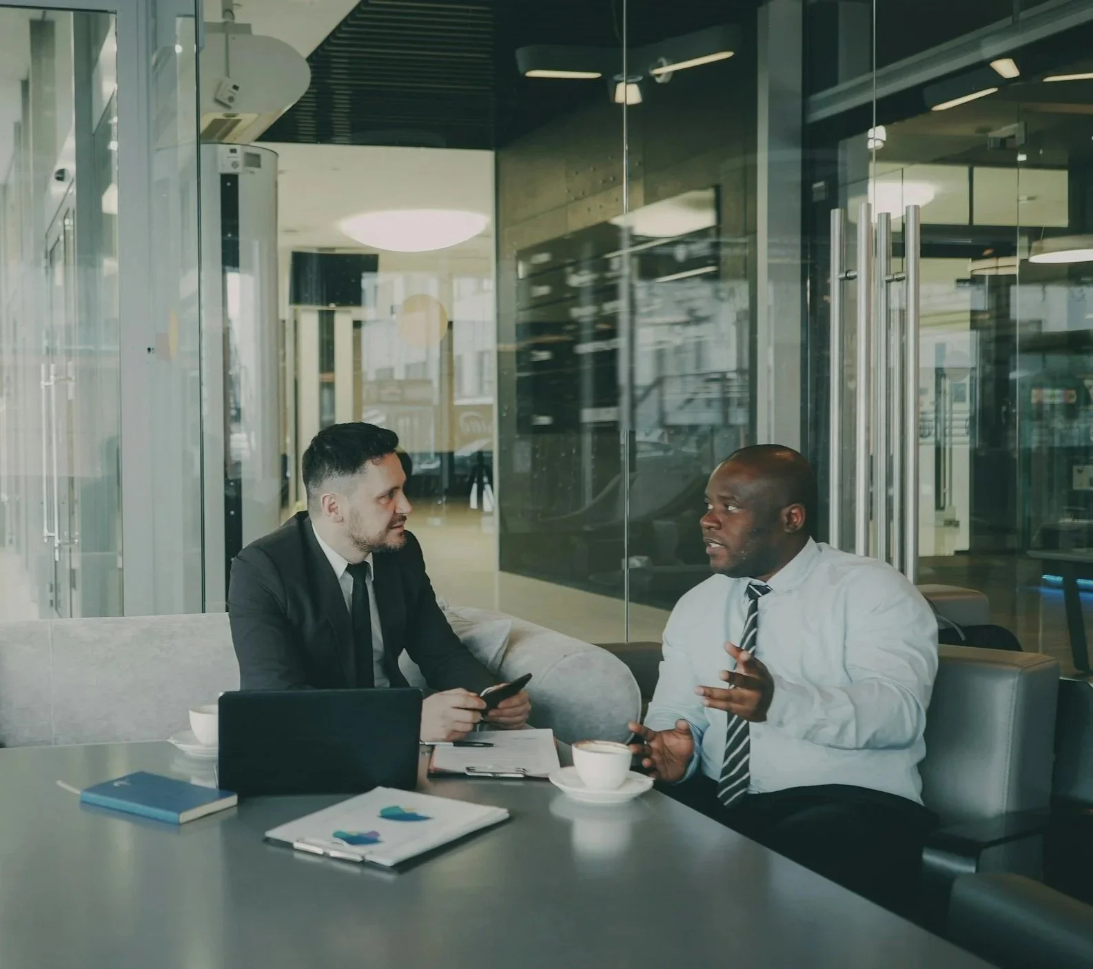 Two men in business attire having a conversation in a modern office cafe.