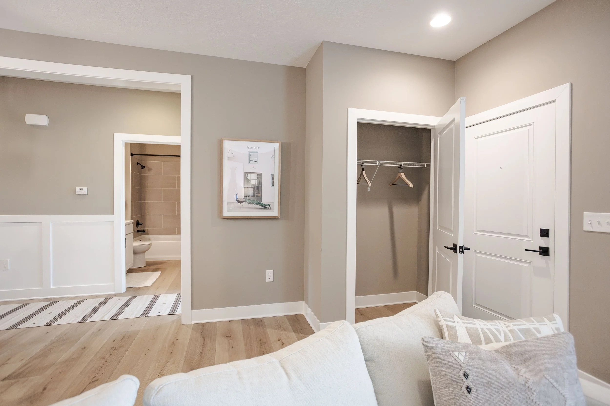 Interior of a modern apartment with an open closet, a door leading to a bathroom, and part of a white sofa with cushions.