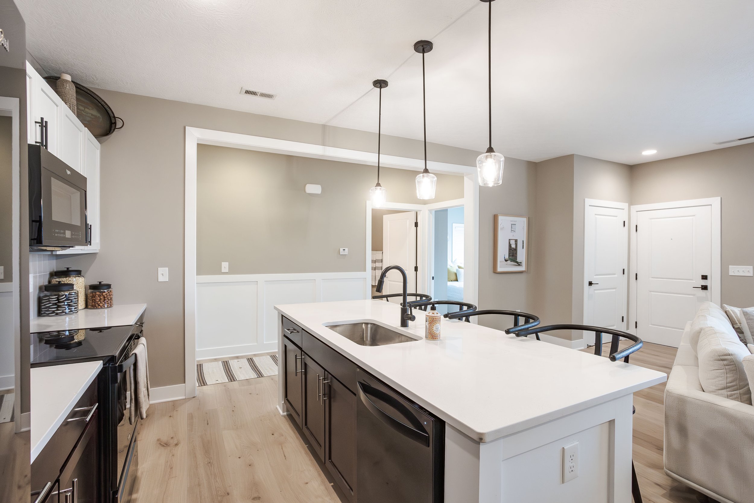 Modern kitchen with white island counter, black cabinets, pendant lights, white walls, and hardwood floors