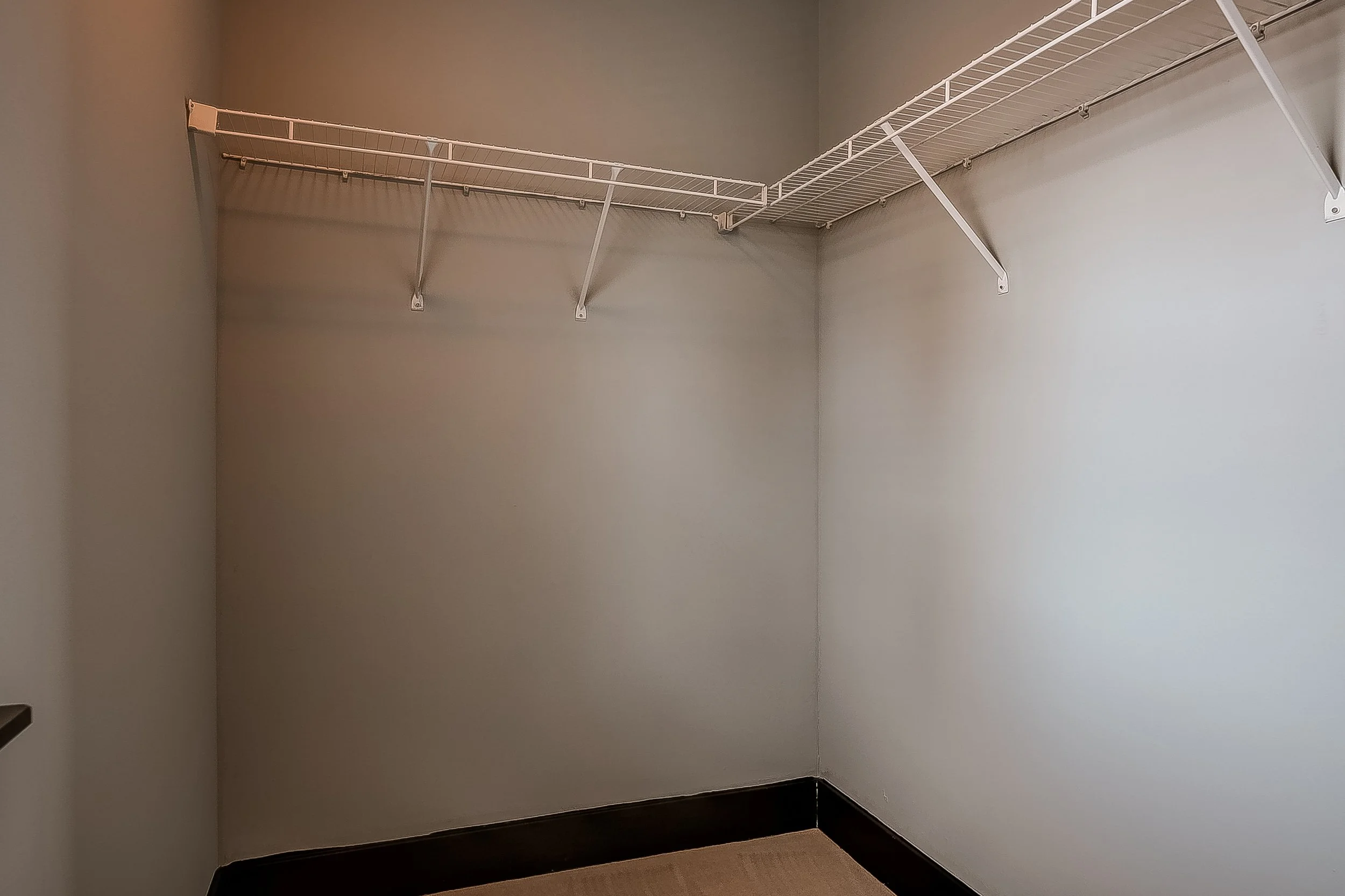 Empty walk-in closet with beige walls and a white wire shelf mounted on the wall.