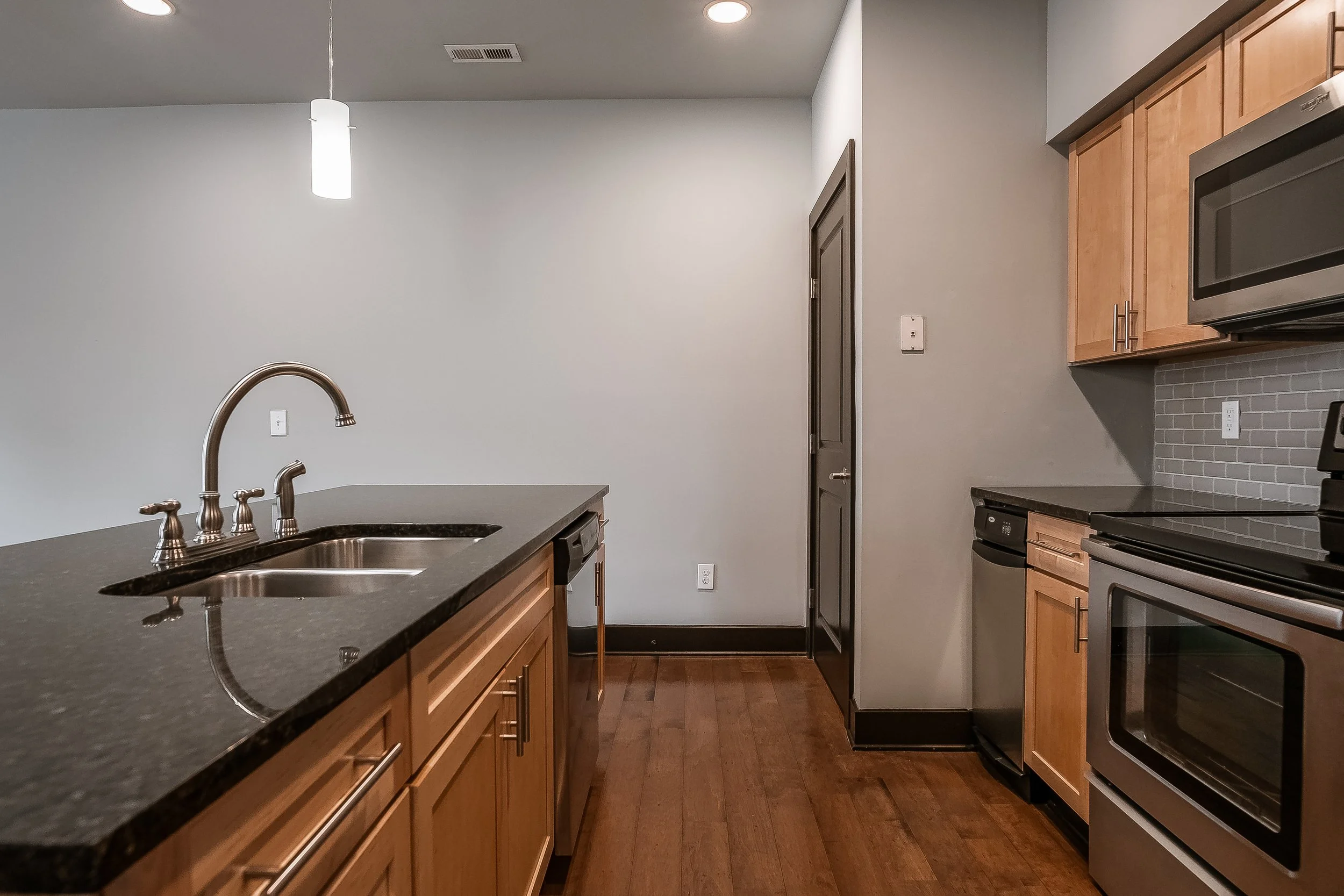 Modern kitchen with black countertop, wooden cabinets, stainless steel appliances, and hardwood flooring.