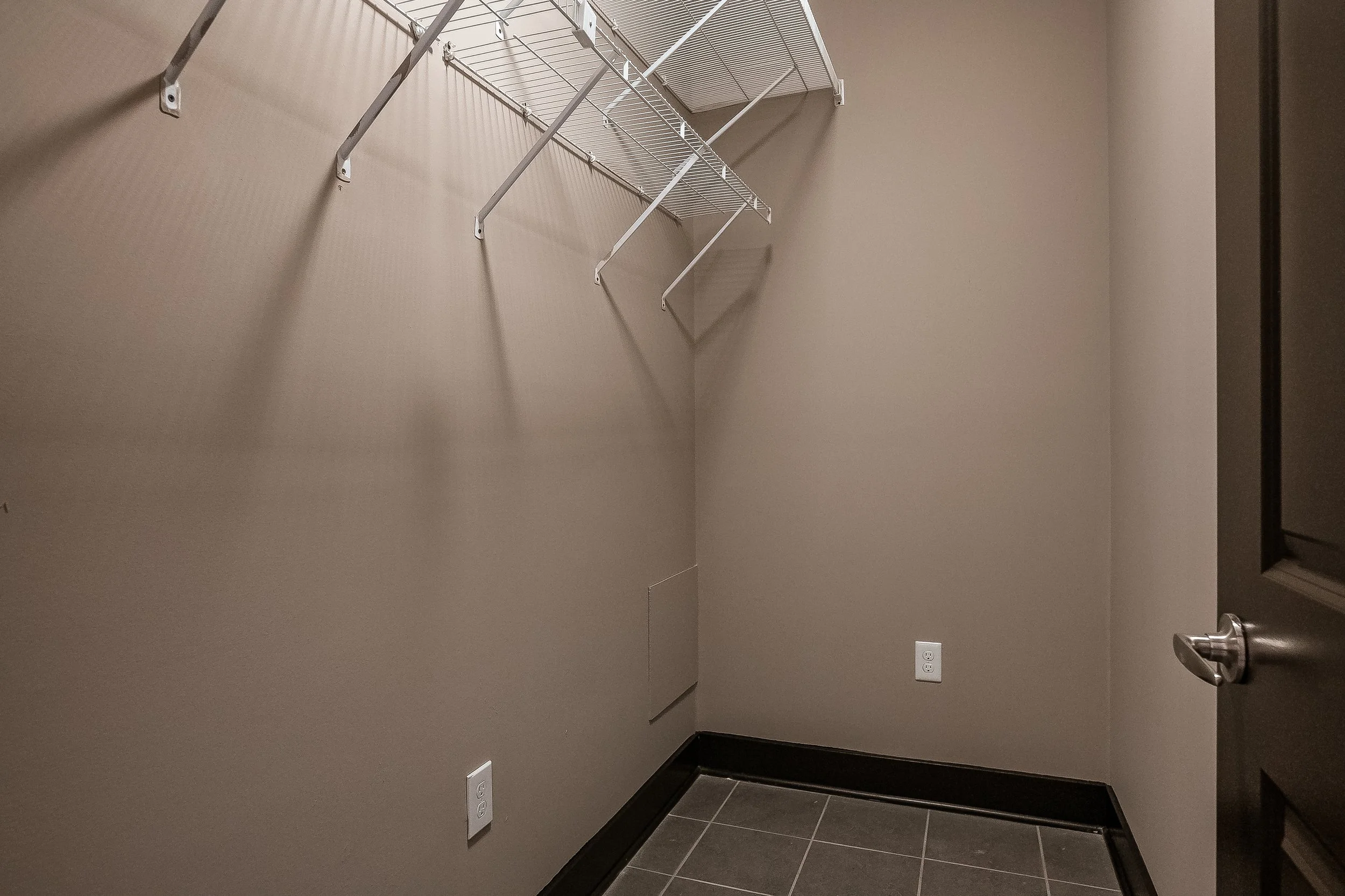 Empty closet with beige walls, wire shelf, and electrical outlets on the wall.