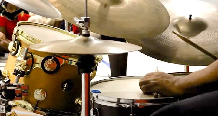 Hands with drumsticks rest on a drumset
