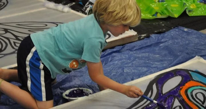 A boy paints fabric on the floor