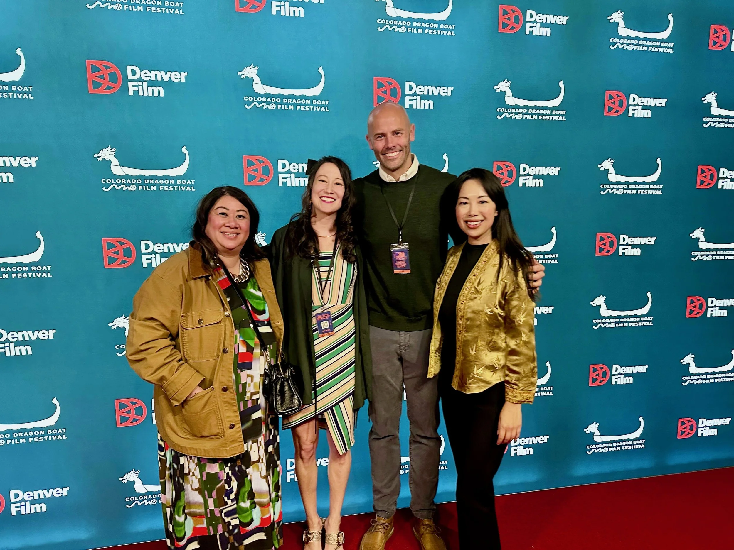 Four people standing together at the Denver Film and Colorado Dragon Boat Film Festival, smiling, posing for a photo in front of a blue backdrop with logos.