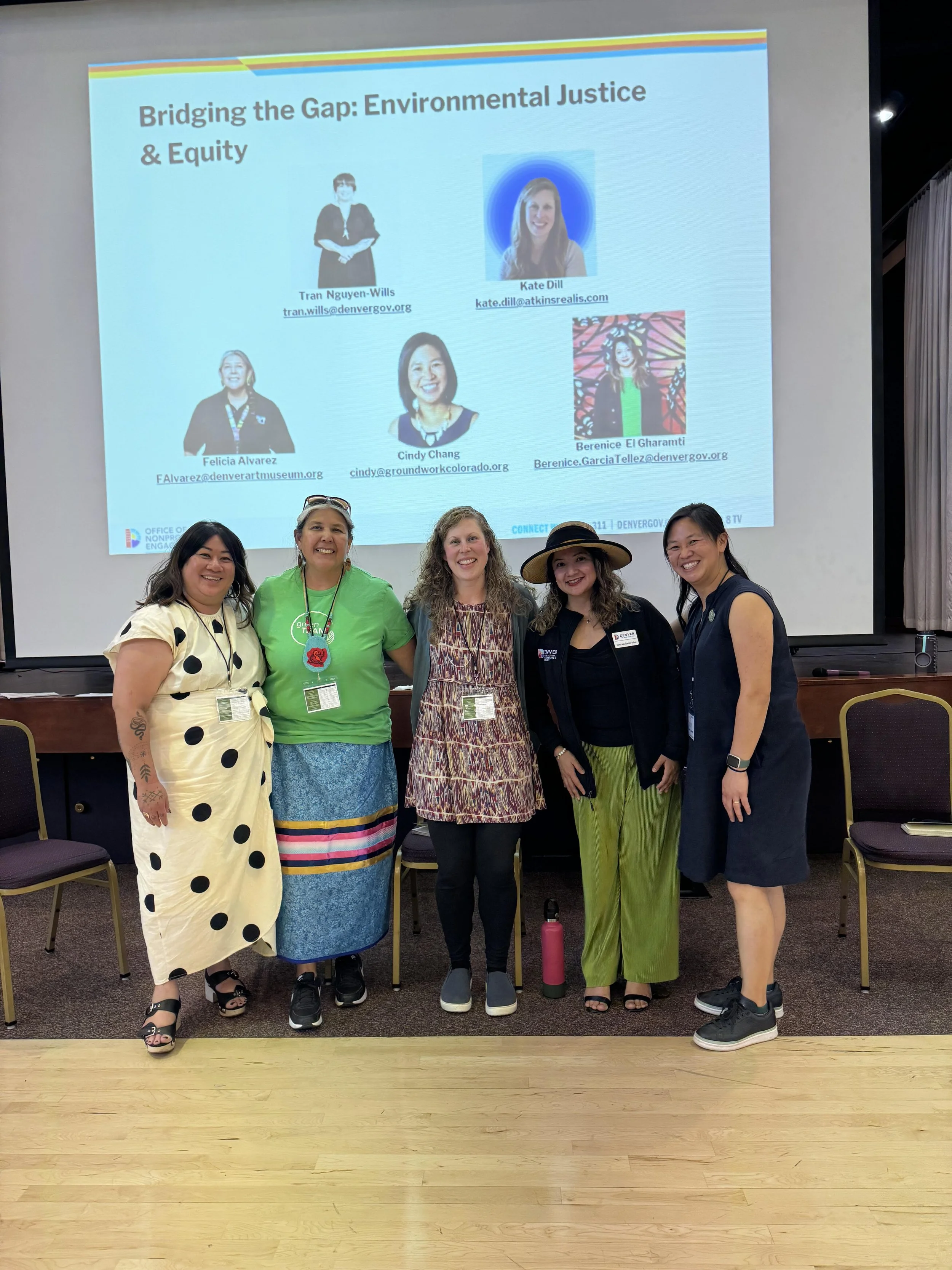Group of five women standing in front of a presentation screen at a conference or workshop. The screen displays a title, "Bridging the Gap: Environmental Justice & Equity," and photos and names of four speakers.
