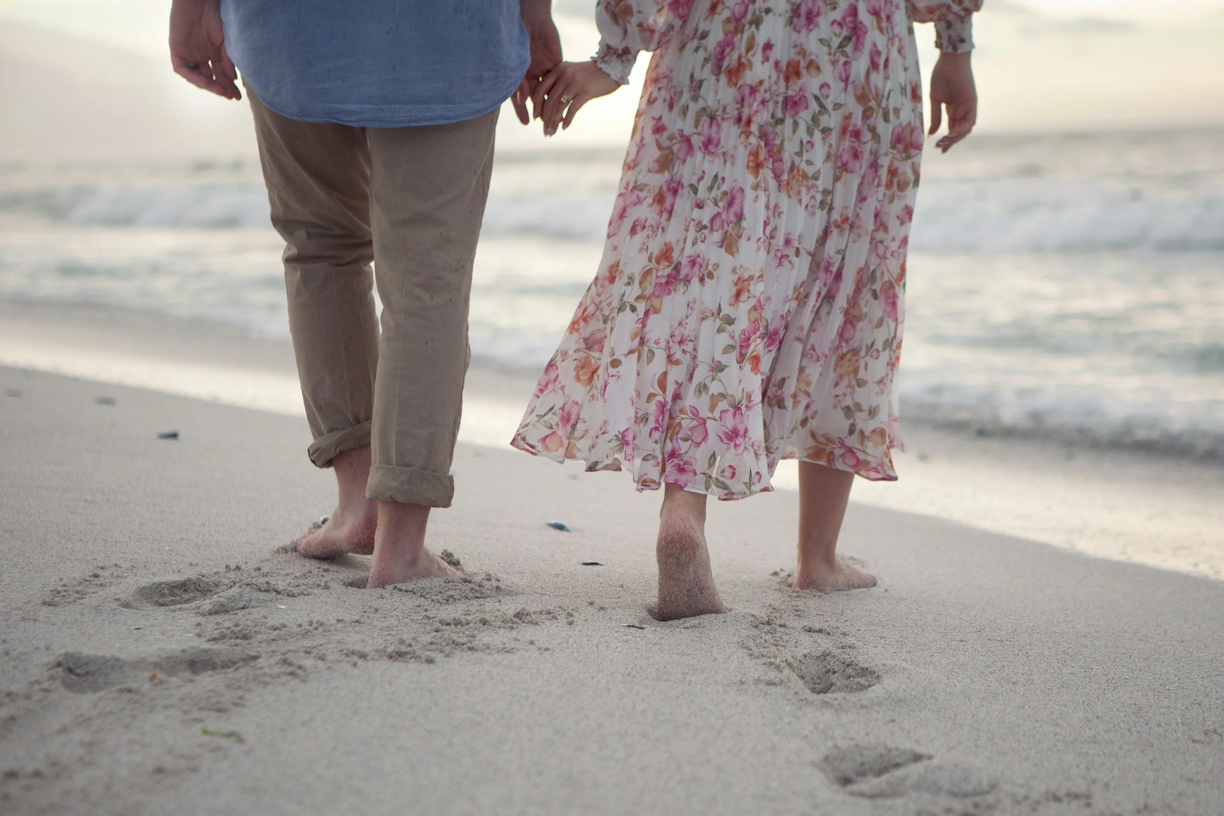 Two people walking on the beach next to the water.