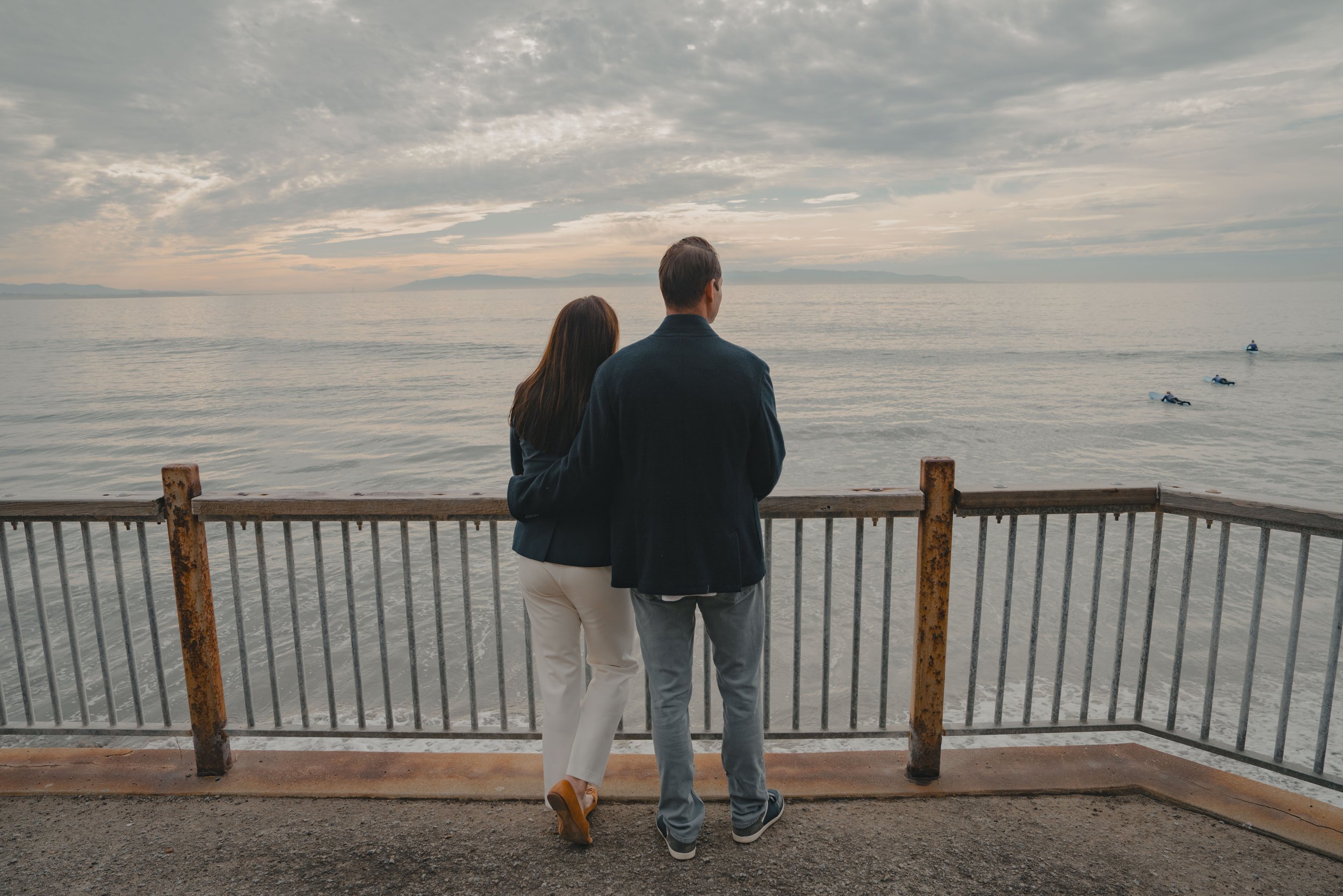 A man and a woman in Capitola Village overlooking the ocean next to a guard rail.