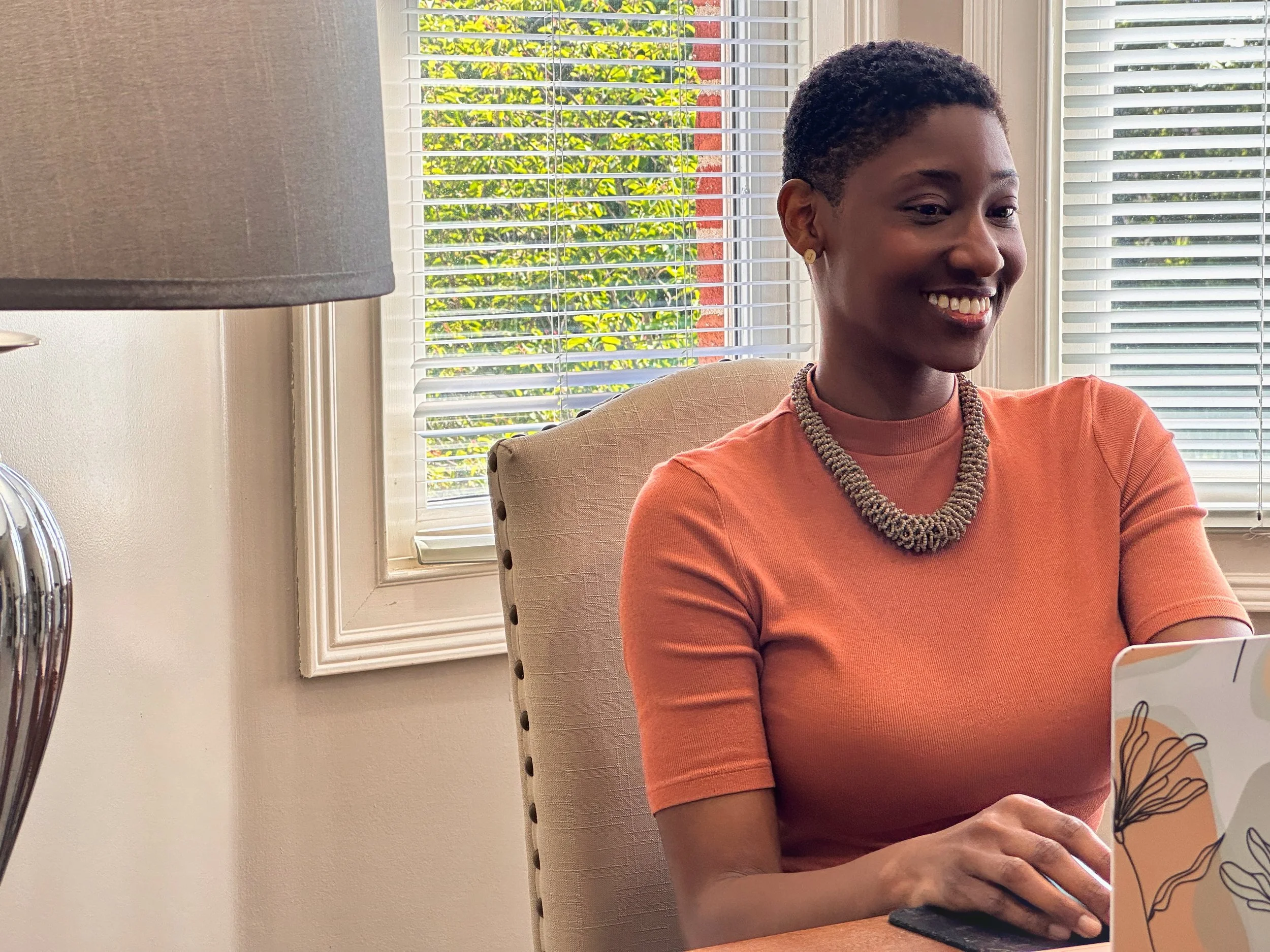Jillian is seated at a windowed corner desk, and working on a laptop.