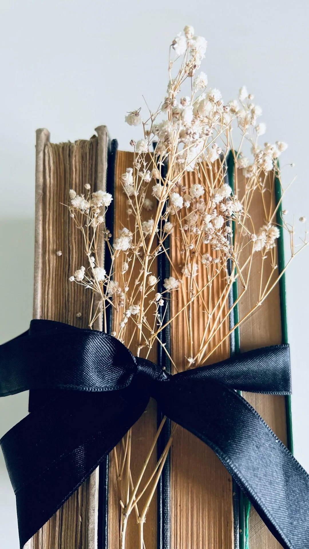 A stack of books tied with a black ribbon, with white dried flowers arranged on top.