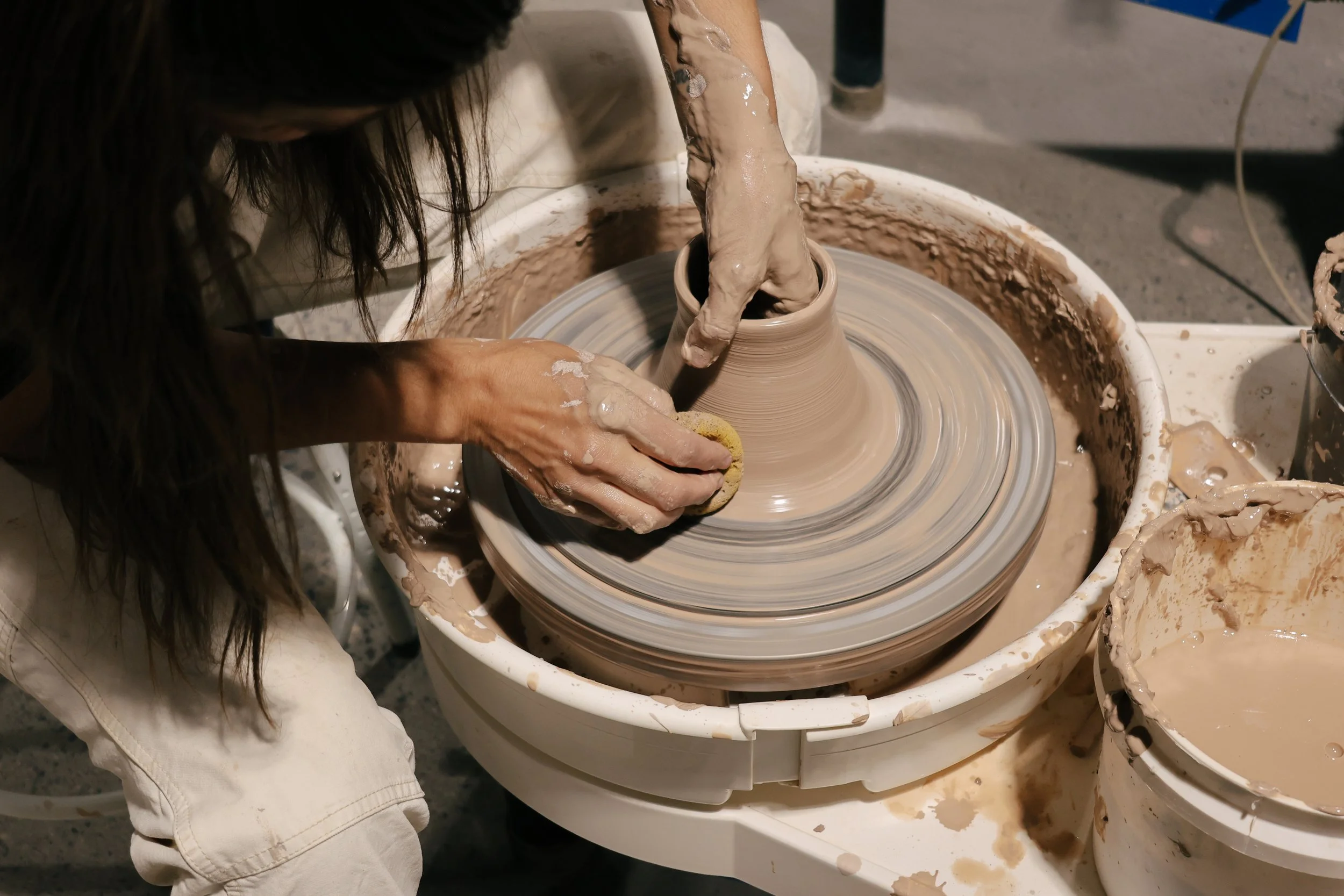 A person shaping a ceramic vase on a spinning pottery wheel with hands covered in wet clay.