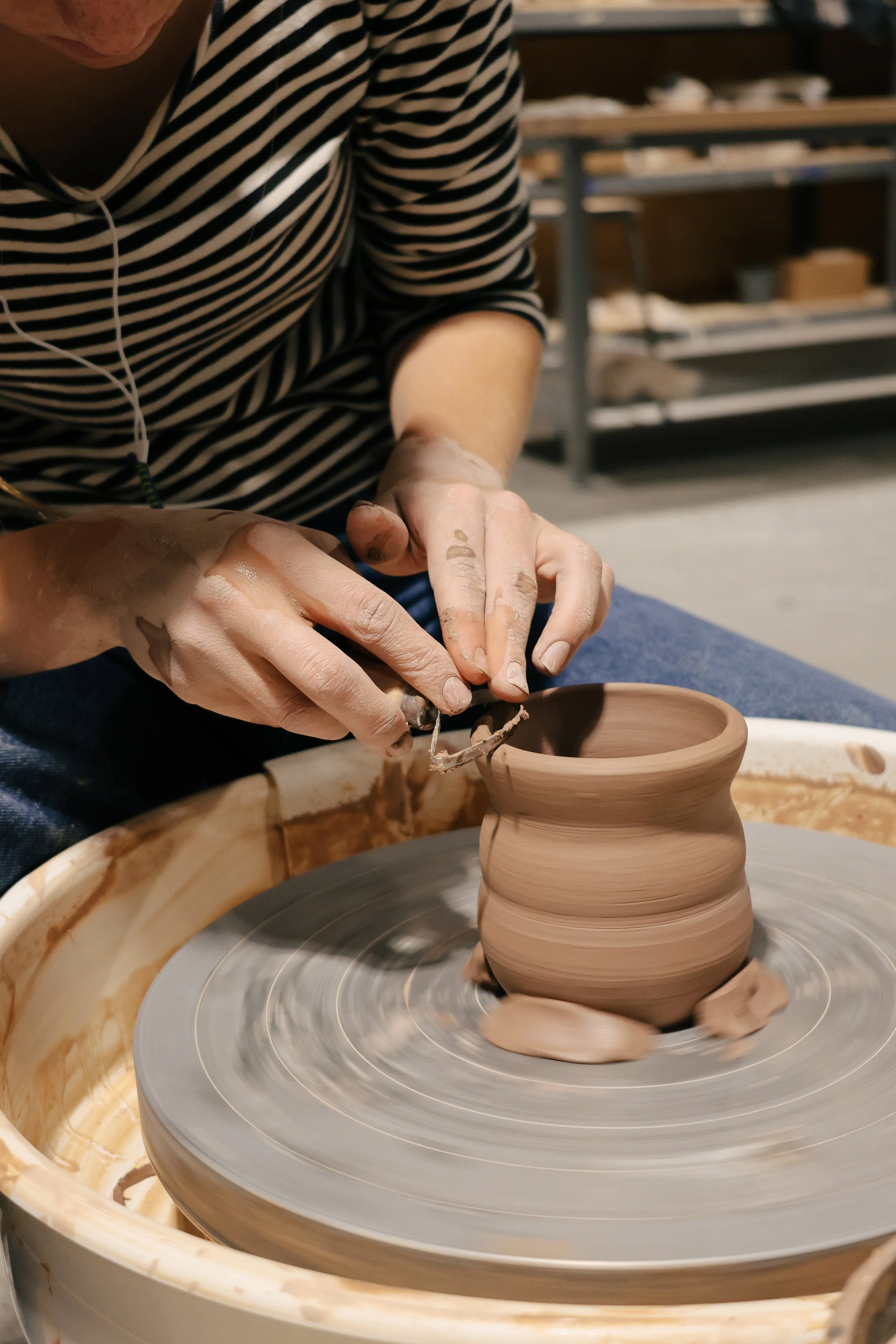 A person shaping clay on a pottery wheel, with their hands covered in clay.