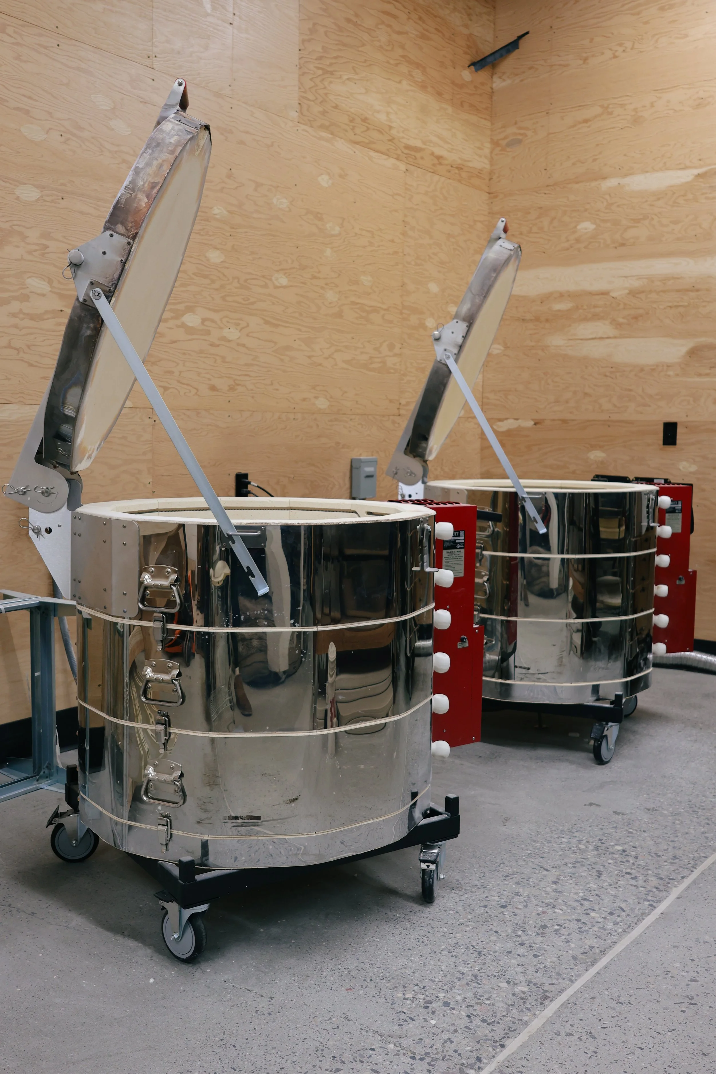 Two robotic surgical arms in a room with wooden walls, mounted on wheeled bases.