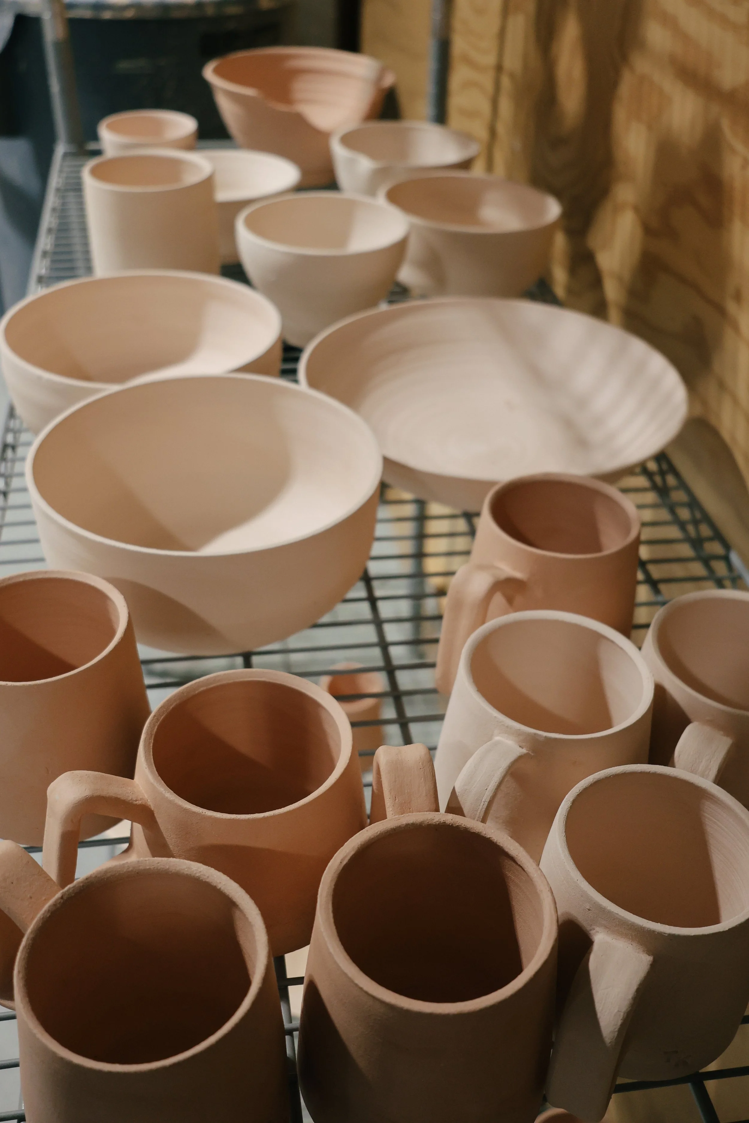 Various unglazed ceramic pots and bowls on a wire rack in a pottery studio.