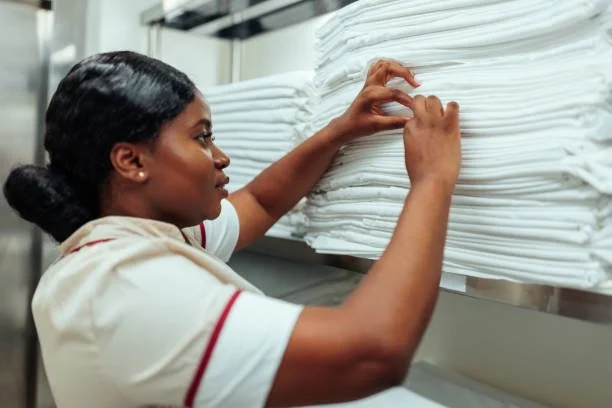 A woman organizing white towels on a shelf in a laundry or linen room.