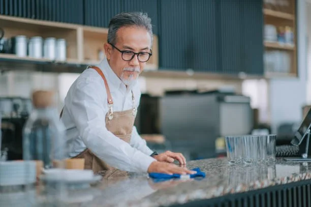 An older man with glasses and gray hair cleaning a countertop in a modern kitchen.