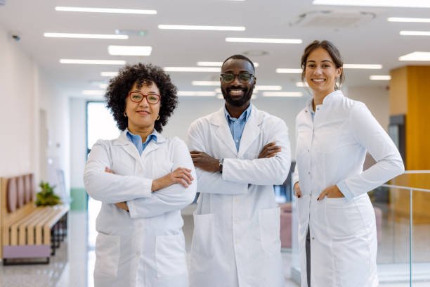 Three healthcare professionals standing together in a hospital or clinic hallway, wearing white coats and smiling.