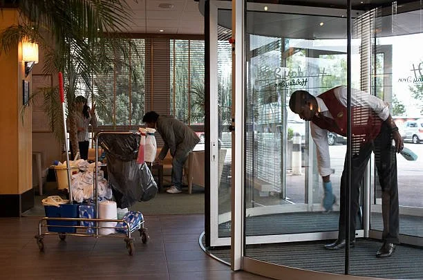 Hotel employees cleaning the lobby, with a cart of cleaning supplies and a person cleaning the glass door.