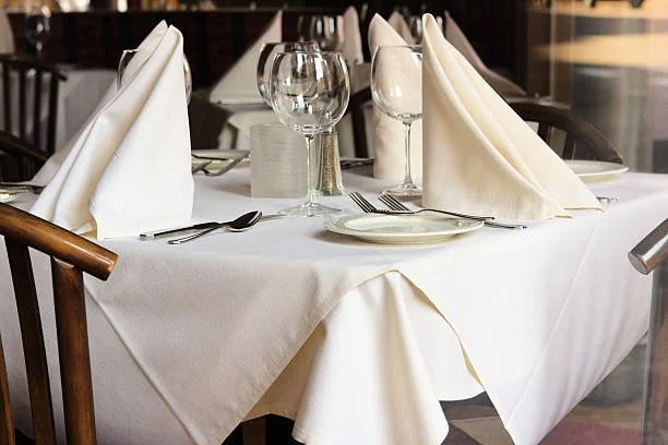 A formal restaurant table set with white tablecloth, folded white napkins, wine glasses, water glasses, plates, and silverware.