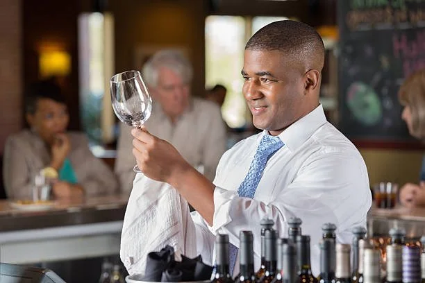 Bartender examining a wine glass at a bar with customers in the background