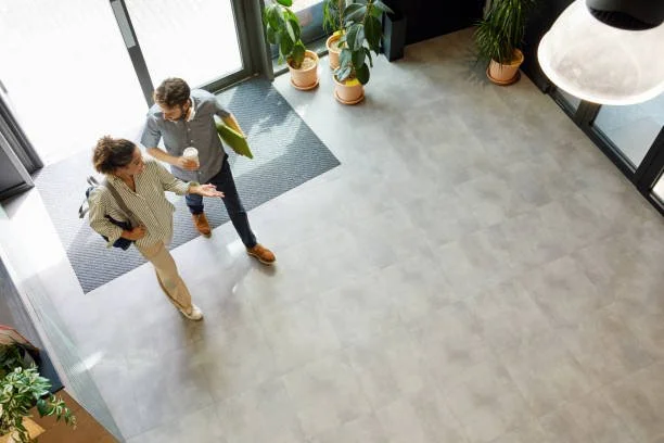 Two people walking and talking inside a modern building lobby with potted plants and large windows.