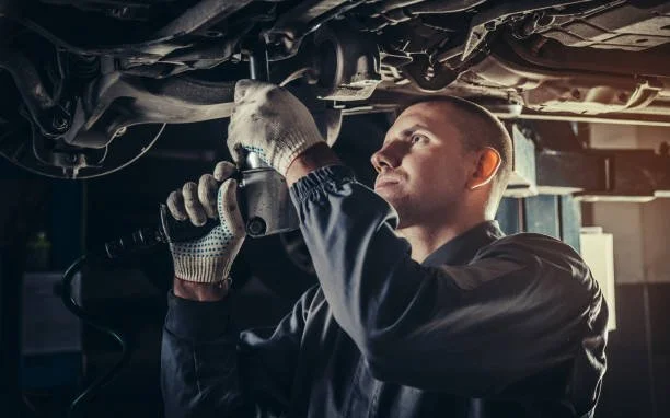 Mechanic working underneath a vehicle with tools in a garage.
