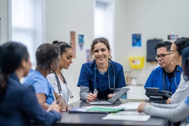 Group of healthcare professionals, including nurses and doctors, having a meeting or discussion in a clinical setting.