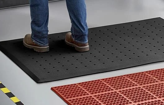 Person standing on a black anti-fatigue mat with a red anti-slip mat nearby in a workspace.