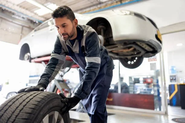 A mechanic working on a tire in an auto repair shop with a vehicle hoisted in the background.
