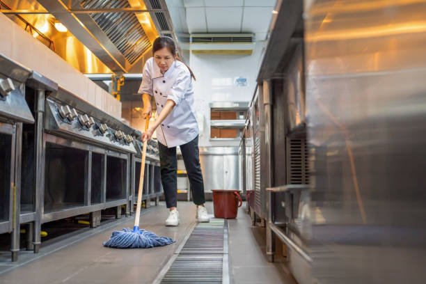 A chef cleaning the kitchen floor with a mop in a professional restaurant kitchen.