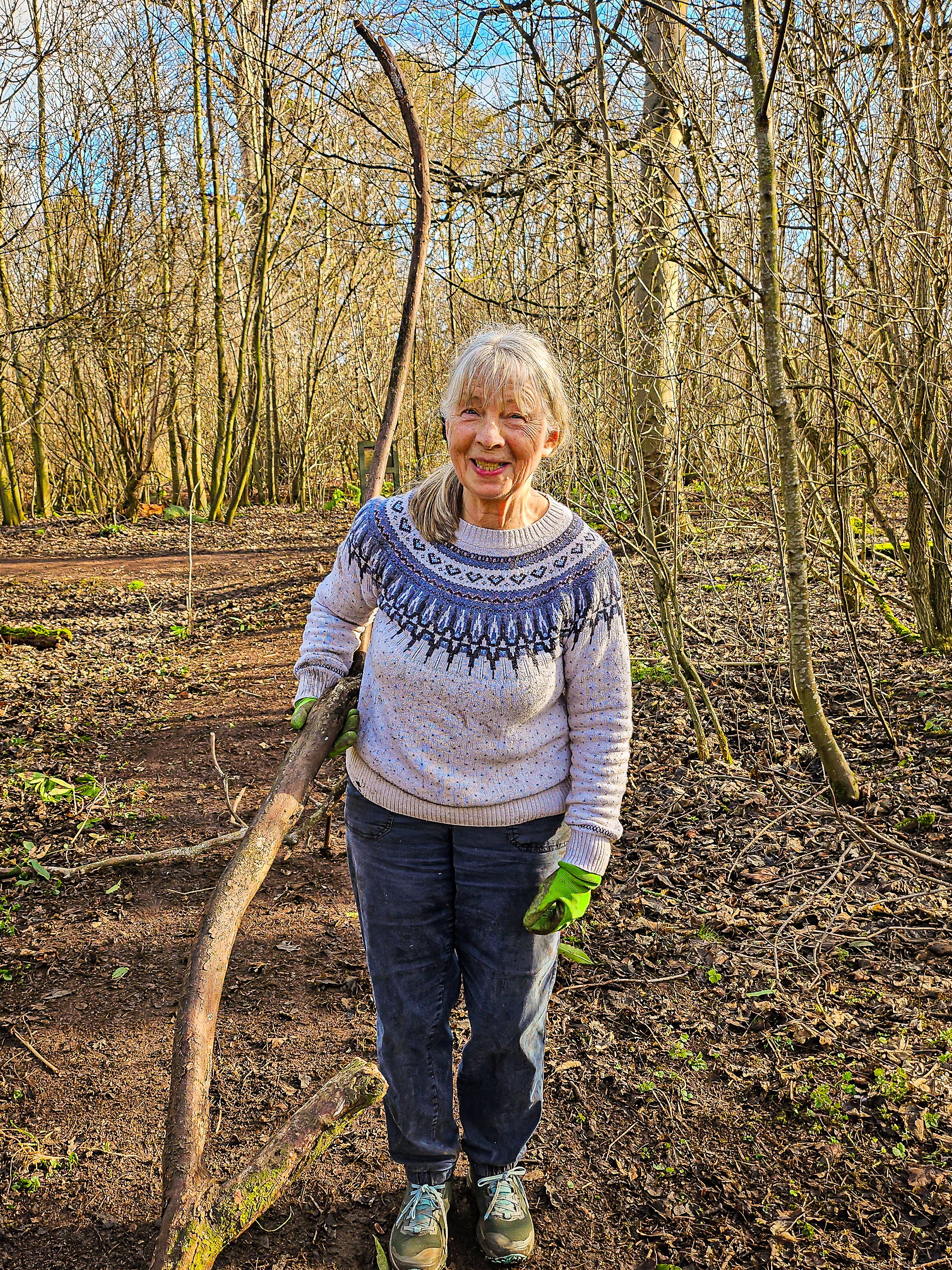 Lady woolly jumper in woods carrying stick sunny