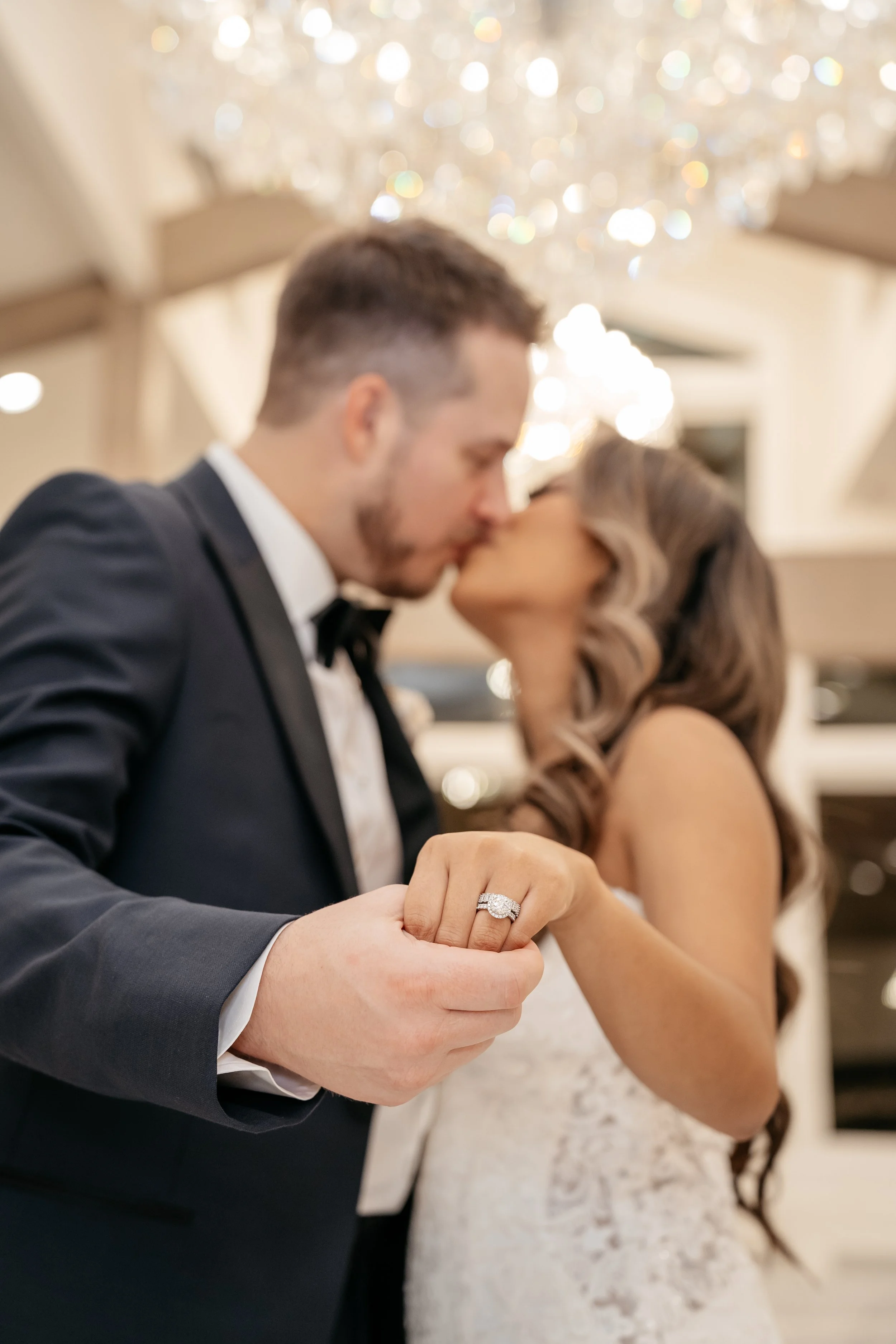 A couple in wedding attire sharing a kiss, with the woman's engagement ring visible on her finger.
