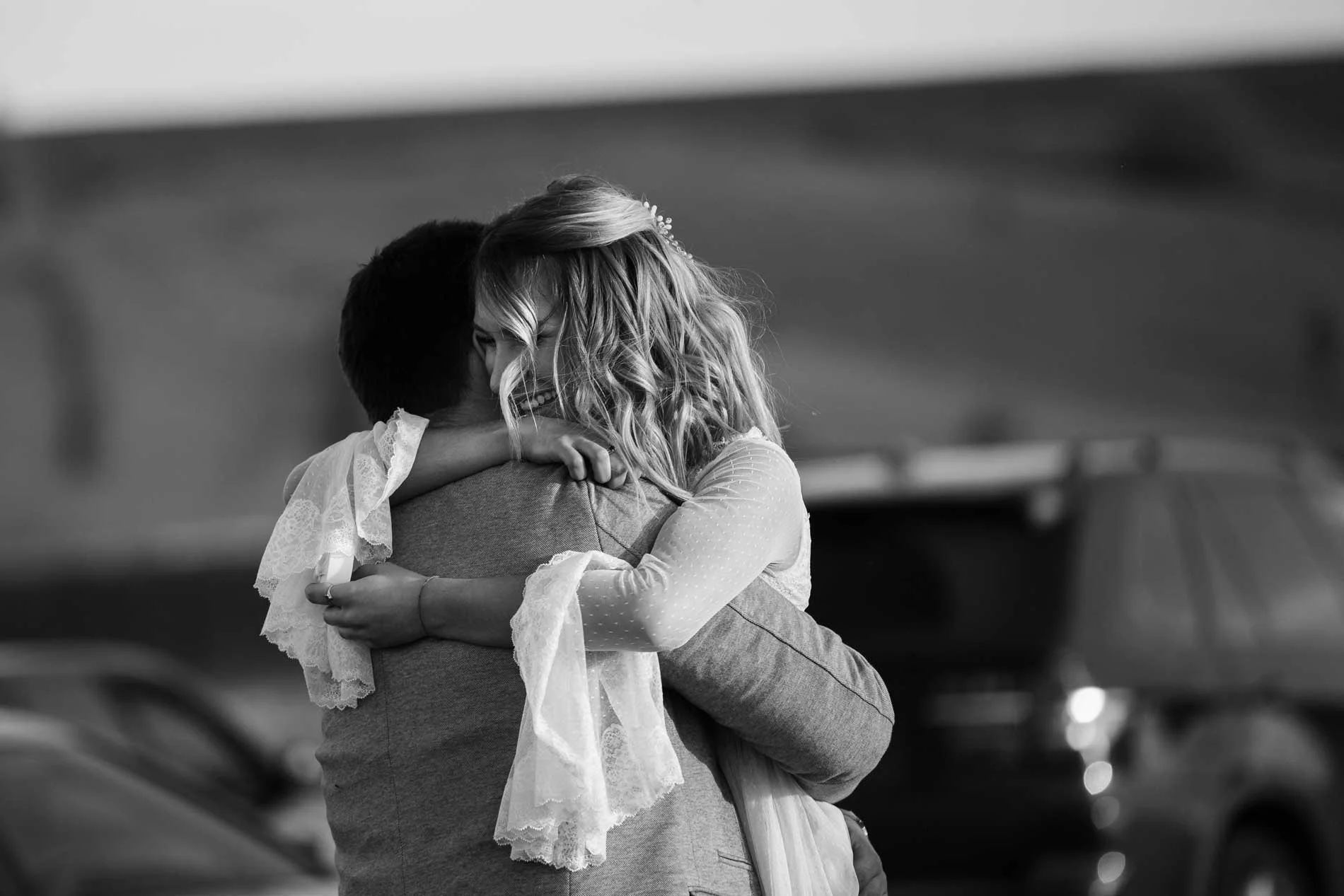 A woman and a child are hugging in an outdoor setting, smiling, in a black-and-white photo.