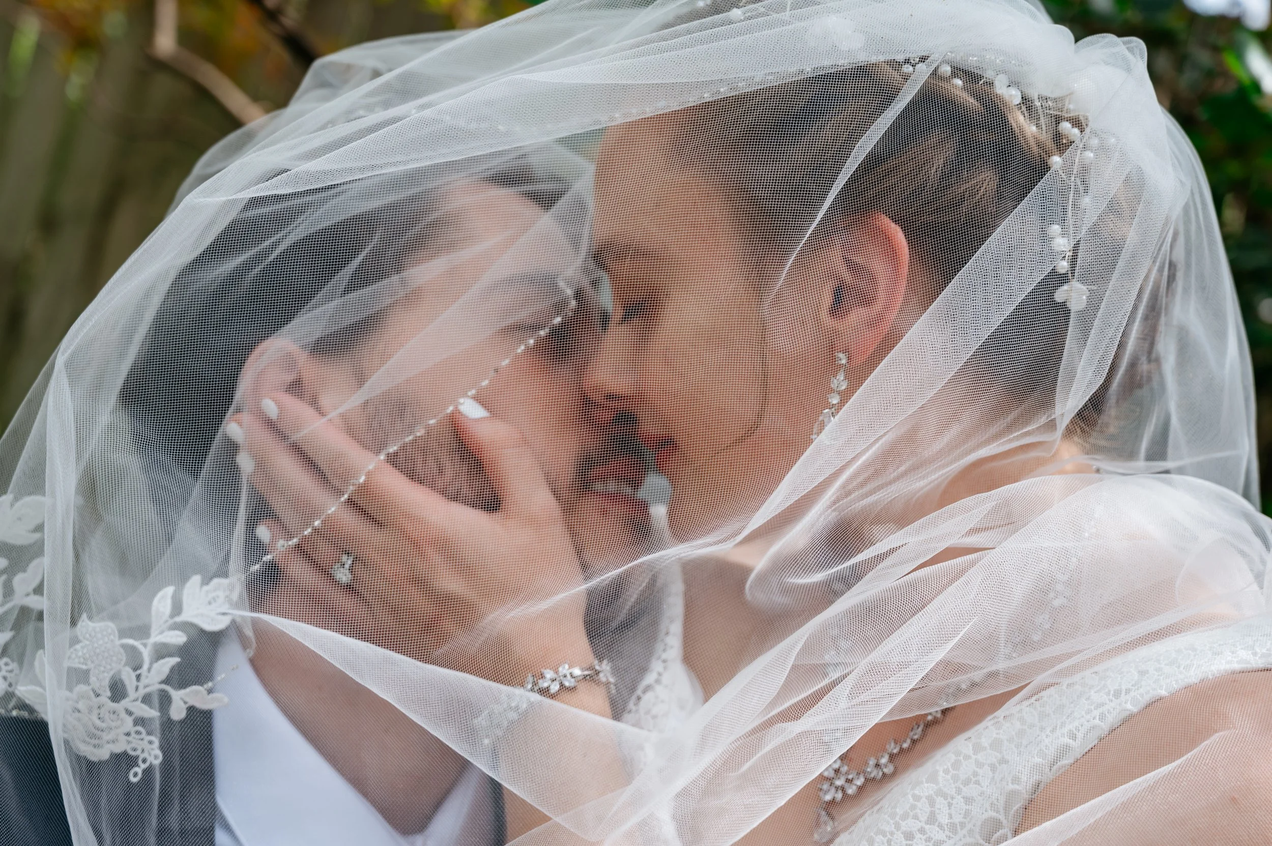 A bride and groom under a wedding veil sharing a close, intimate moment.