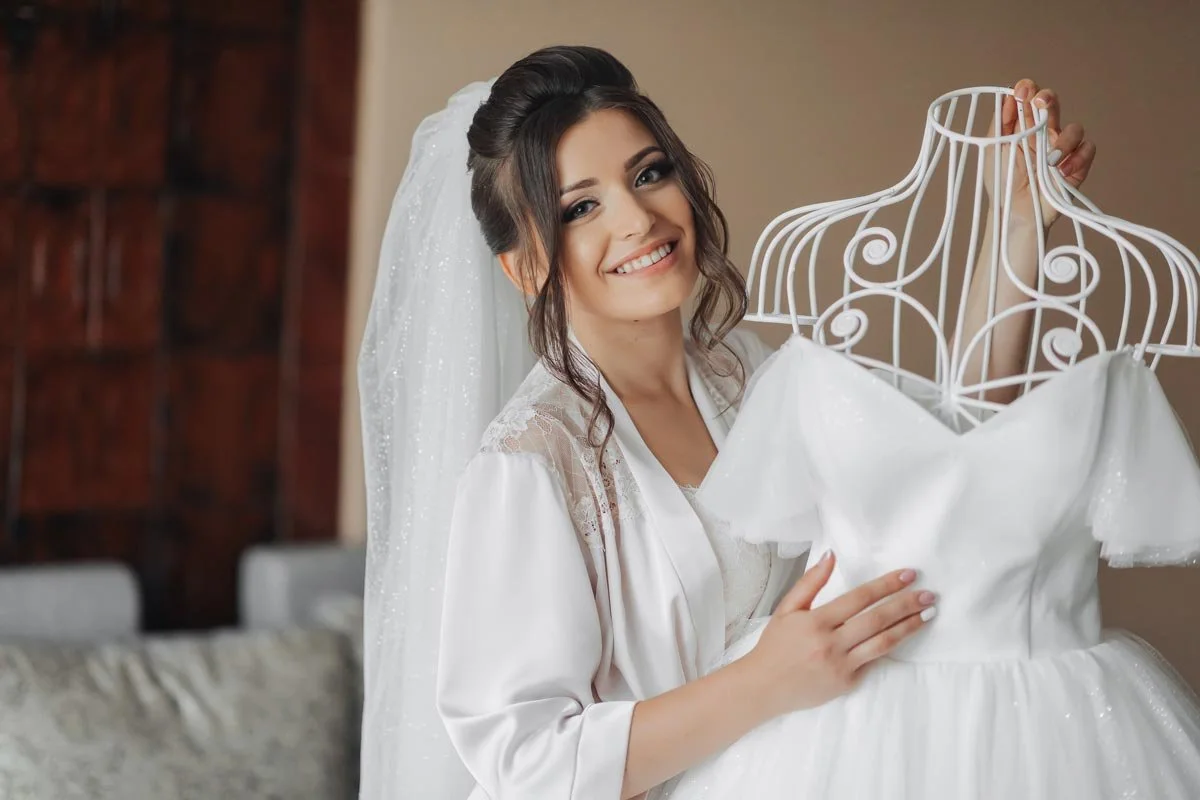 Bride holding her wedding dress on a decorative hanger, smiling during bridal getting-ready moments
