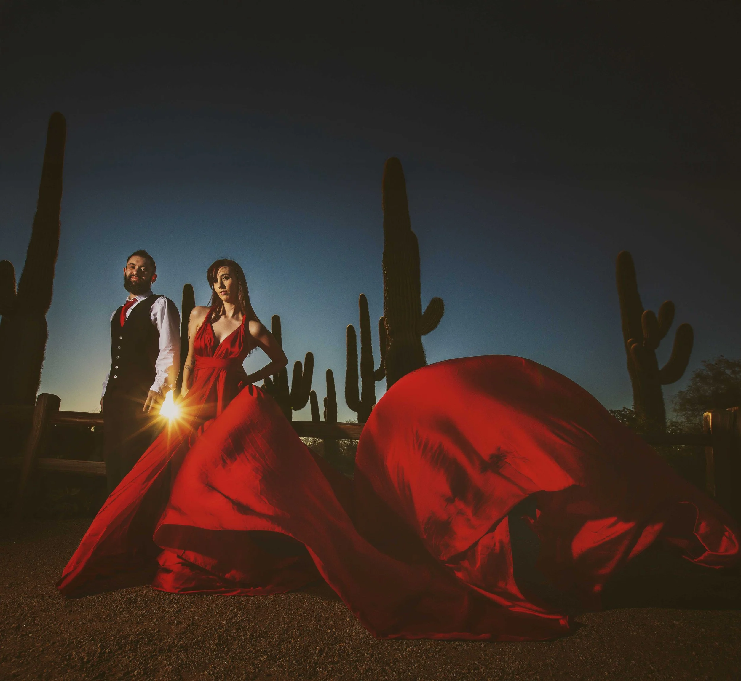 photo of  a couple dressed top notch with the lady in a red flying dress and cactus in the background