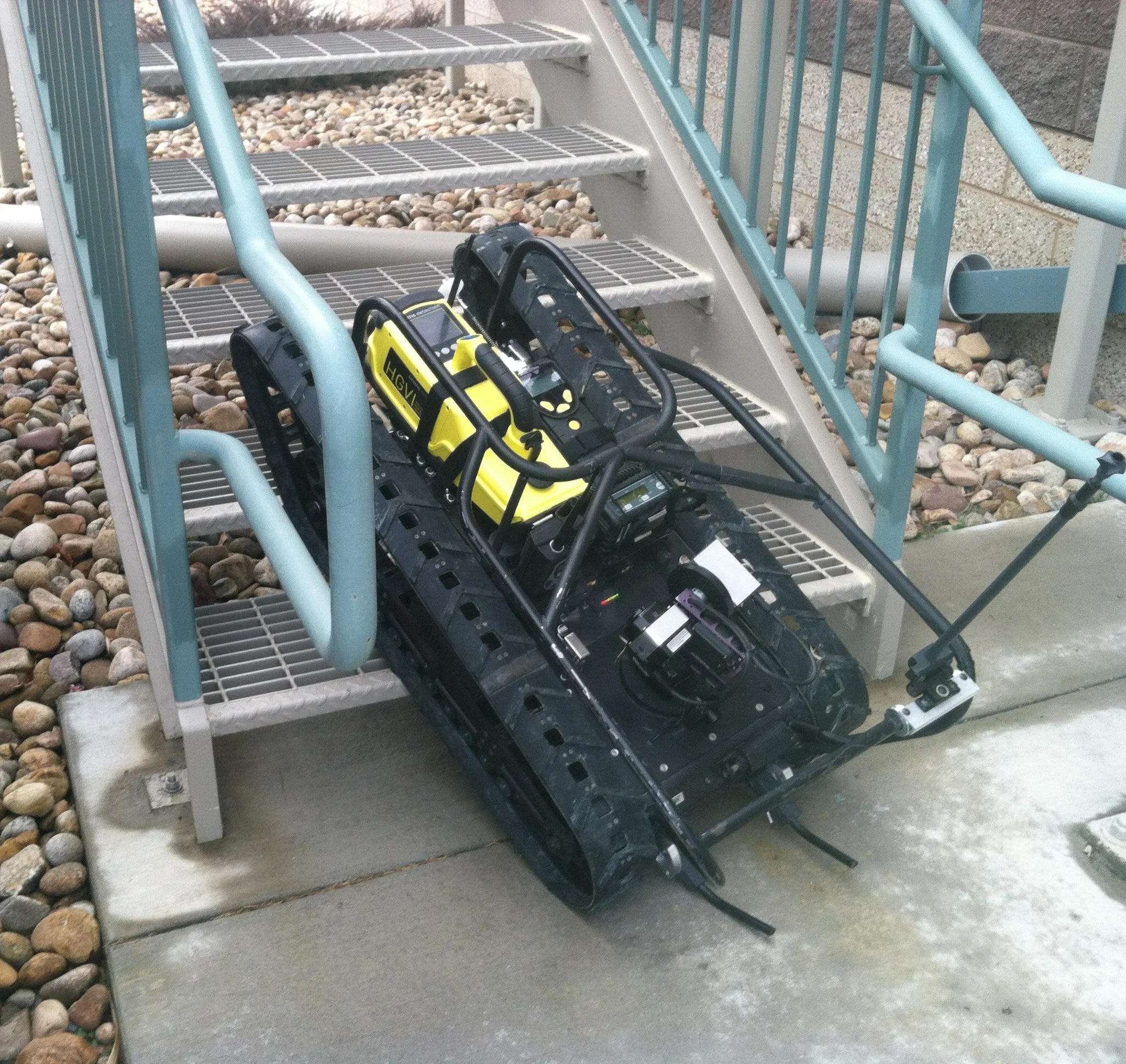 An MMP-40X EOD robot with gas sensors resting on the steps of a metal staircase outside. 