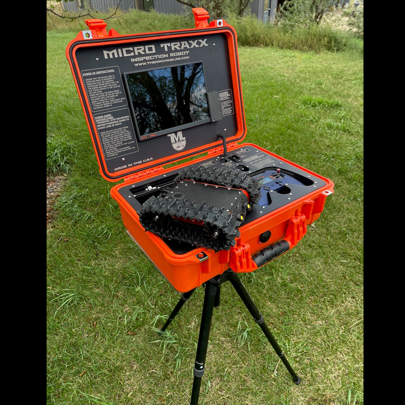 A bright orange portable inspection robot case open on a tripod stand outdoors, containing a small control screen and an all-terrain tracked robot device inside.