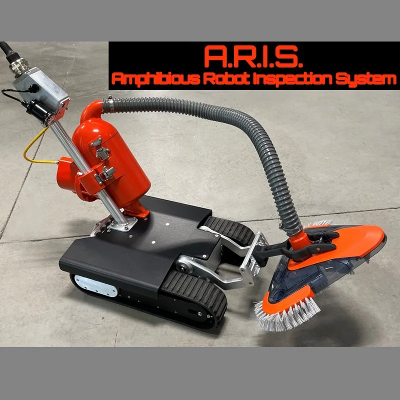 A robot with treads, an orange and black body, and a hose extending from its back, equipped with a brush attachment in front, part of the Amphibious Robot Inspection System (A.R.I.S.).