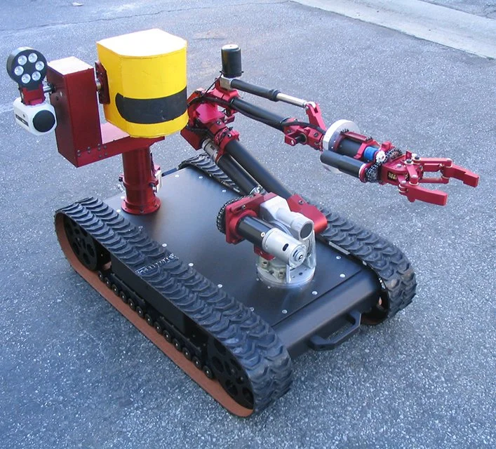 A small tracked robot with a red and black color scheme, equipped with mechanical arms and sensors.