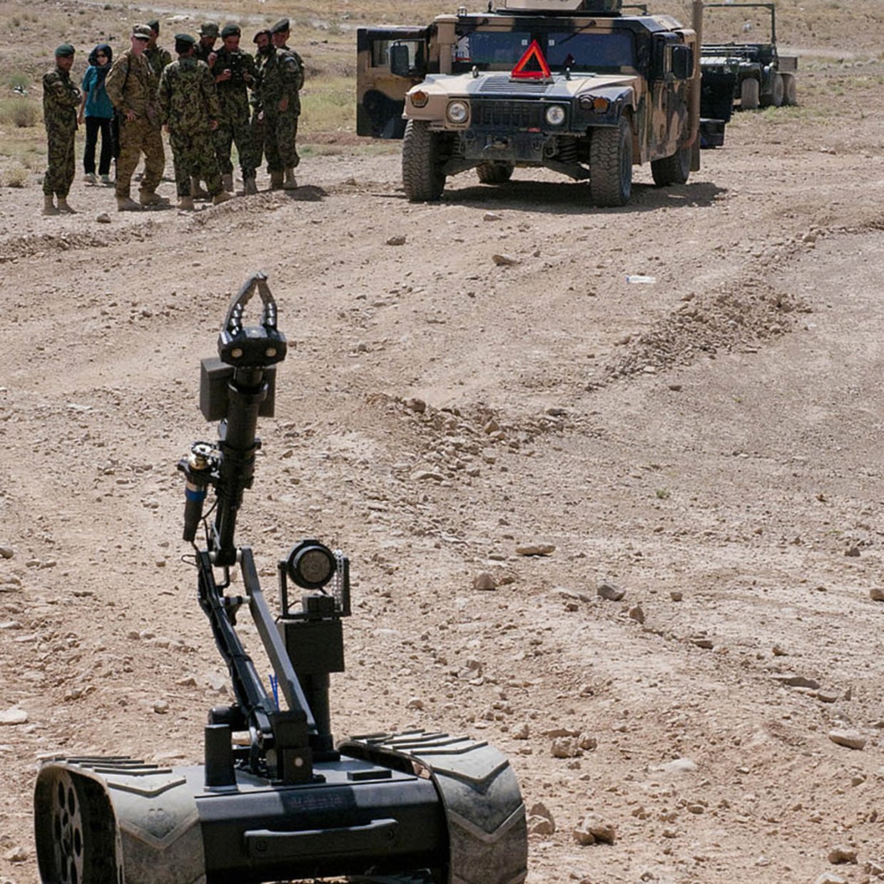 Military personnel in desert terrain with a military vehicle, an MMP-30-EOD rover, and a robotic device in the foreground.