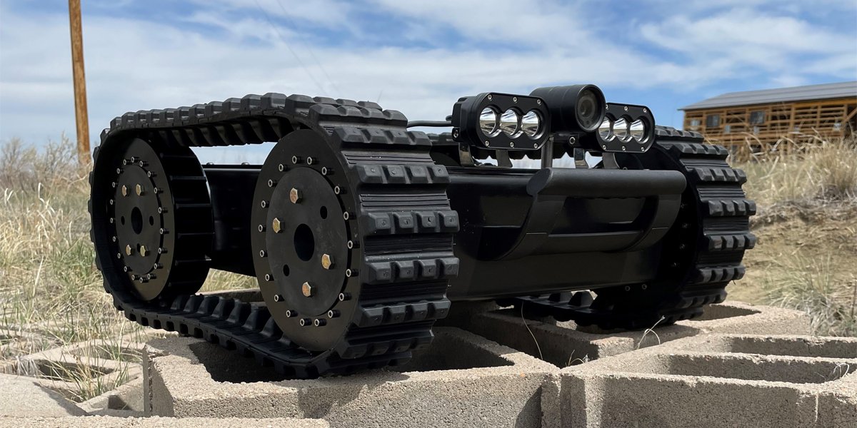 A black robotic tank with caterpillar tracks, a camera and lights, on a concrete block outdoors.