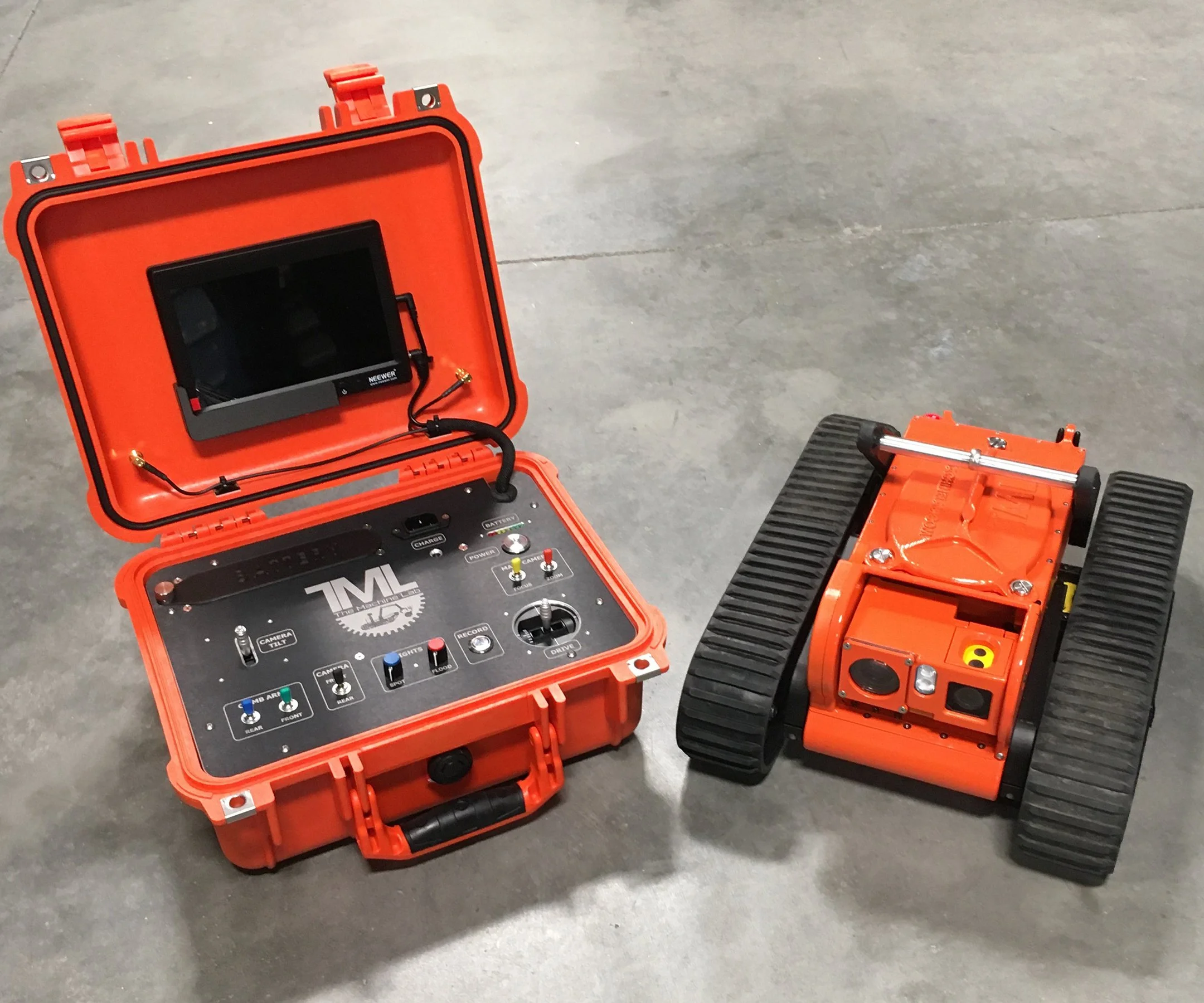 The Glimpse inspection robot with orange and black tracks and a black and orange body, placed on a gray concrete floor, alongside an open orange case containing a remote control and electronic equipment.