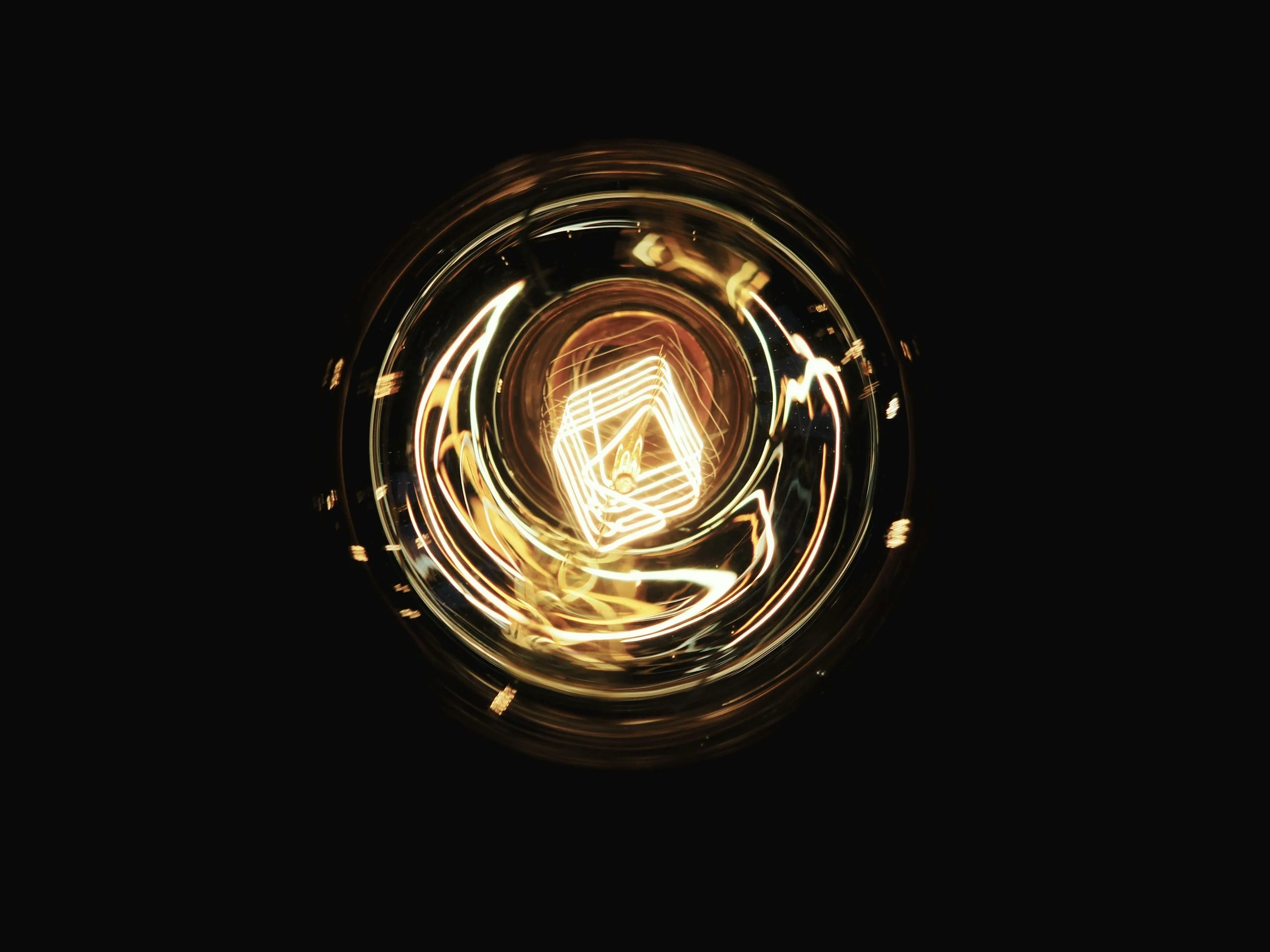 Close-up of a vintage Edison-style light bulb filament glowing with warm amber light, against a black background.
