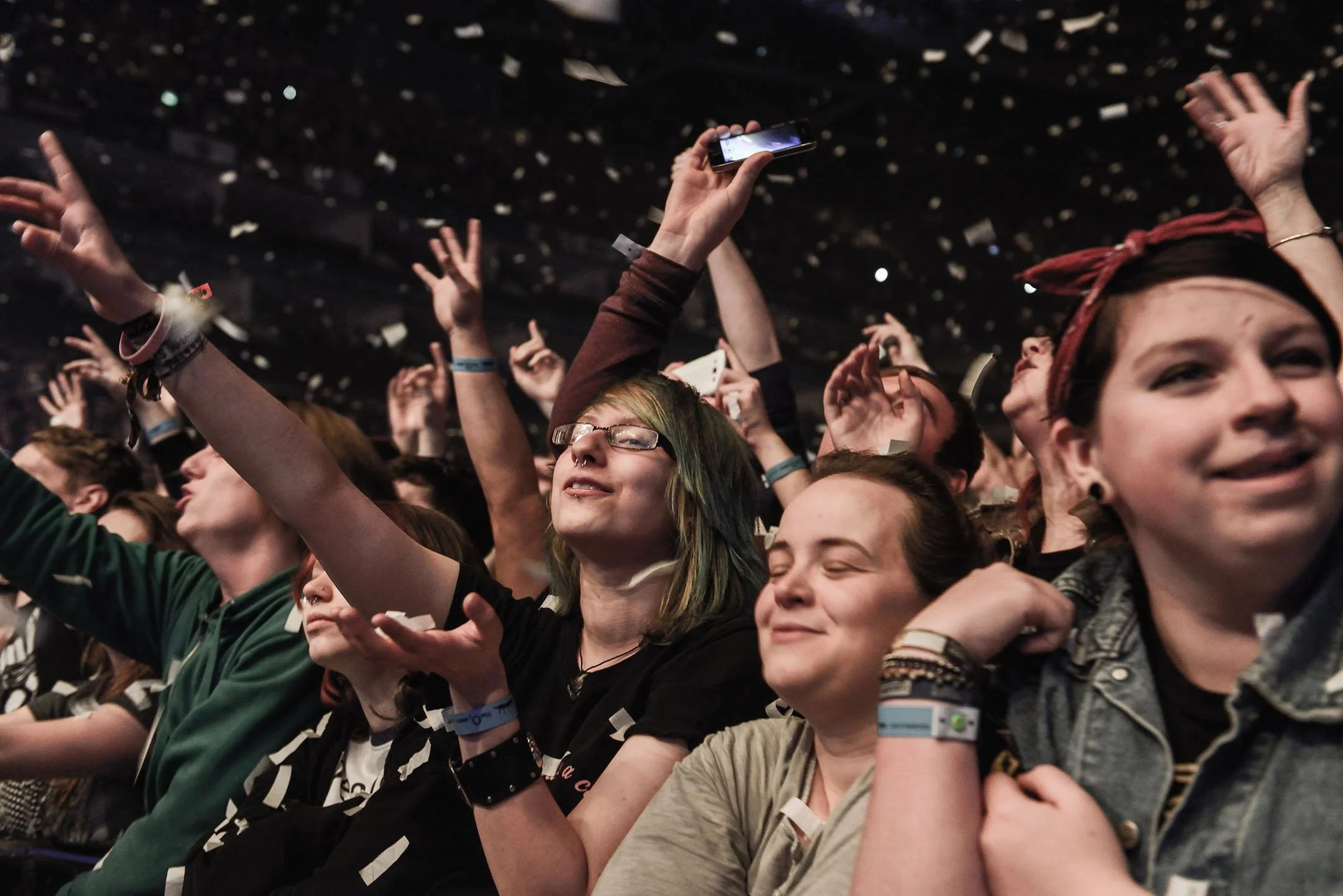 Crowd of young people at a concert, with some raising their hands, closed eyes, and smiling.